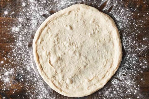 A round of stretched pizza dough on a floured counter